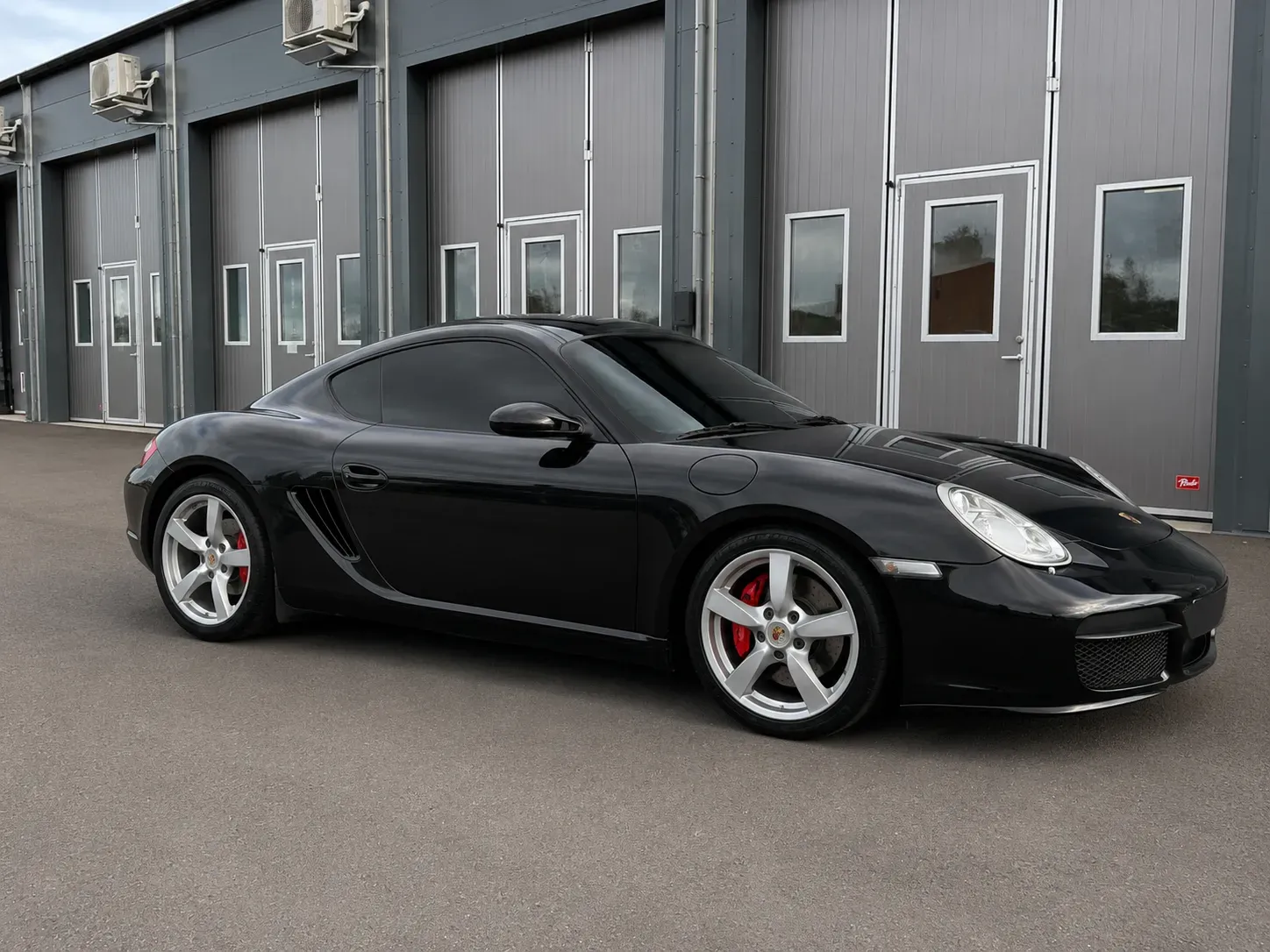 Svart Porsche Cayman med tonade rutor efter professionell toning med solfilm utanför verkstad i Skövde.