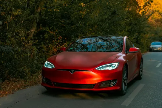 Röd Tesla med stenskottsskydd på en väg i höstljus
